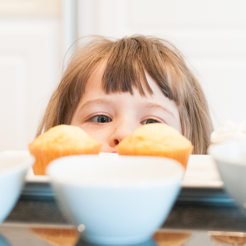 cute face peeking over two undecorated cupcakes, Plymouth MI Child Photography
