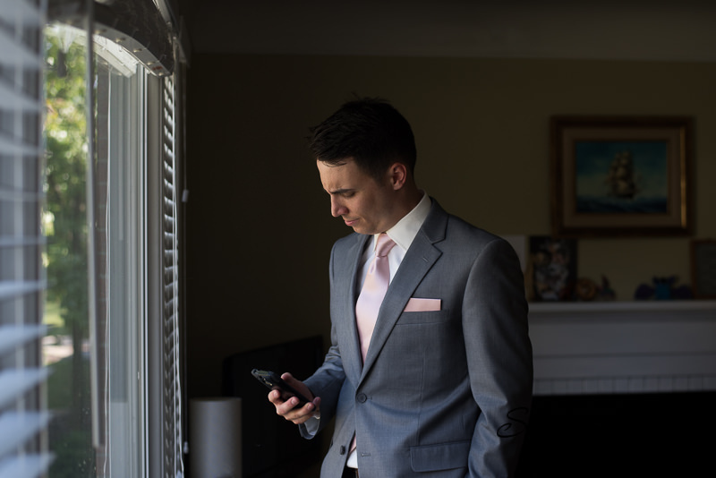 Groom checking his phone on his wedding day, Livonia Documentary Wedding Photography